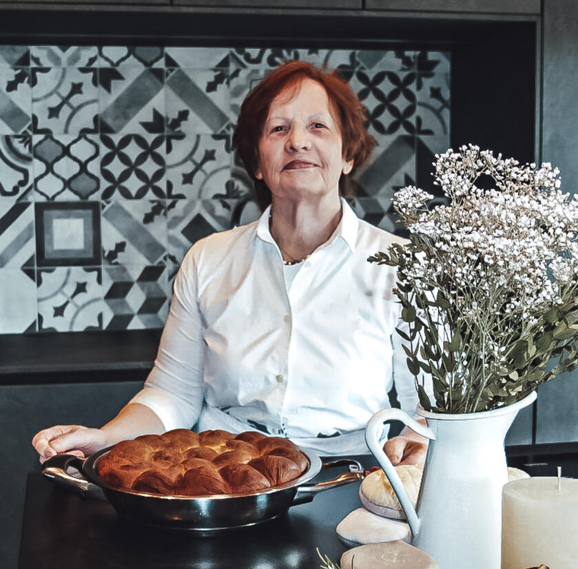 Ältere Frau steht mit traditionellem Tiroler Gericht in der Küche