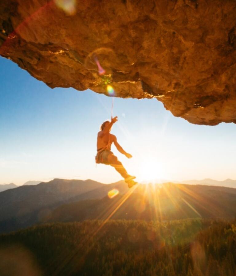 Mann hängt am Kletterseil an einem Felsen