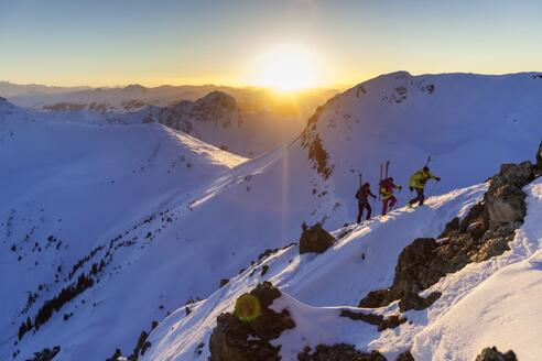 Drei Skitourengeher wandern auf einen schneebedeckten Gipfel