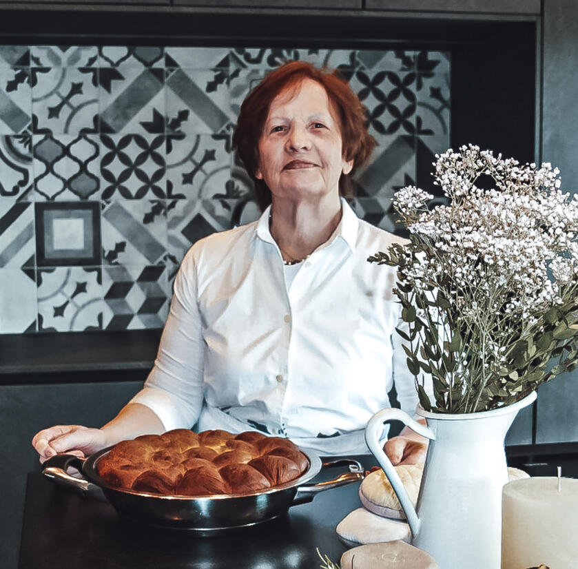 Oma Vroni Hotel Chalets Grosslehen Ältere Frau steht mit traditionellem Tiroler Gericht in der Küche