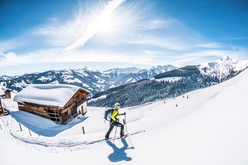 Ein Skitourengeher geht im Tiefschnee bei einer Hütte vorbei